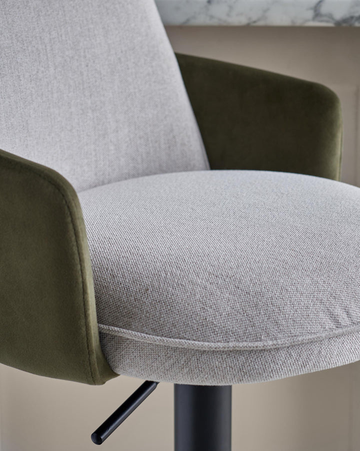 Close-up of a stylish, modern bar stool with grey fabric seat and backrest, plus green armrests and a black metal base.