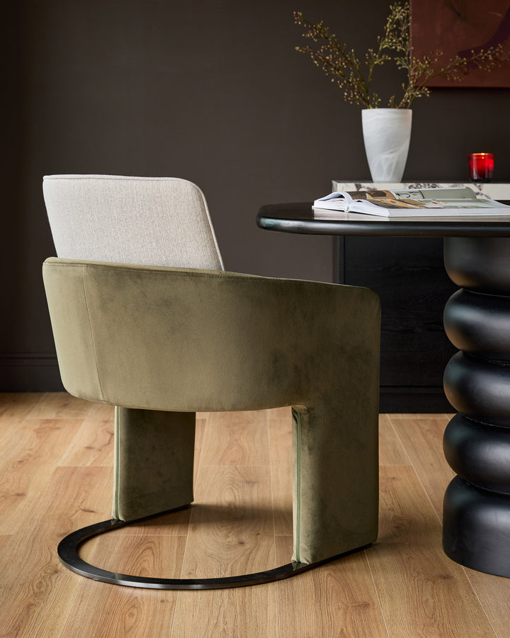 Wren cantilever dining chair in natural and olive green velvet, shown from rear angle in styled room setting.