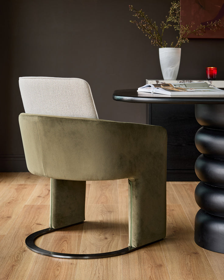 Wren cantilever dining chair in natural and olive green velvet, shown from rear angle in styled room setting.