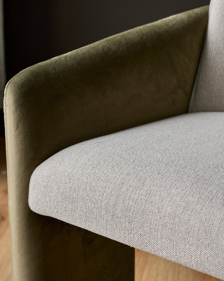 Wren cantilever dining chair close-up showing olive-green velvet backrest and natural fabric seat cushion.