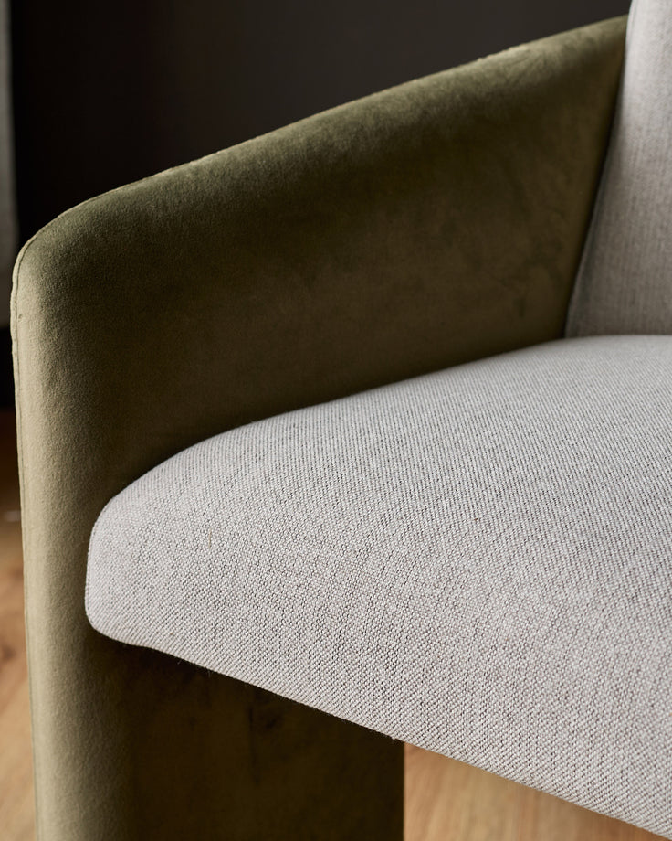 Wren cantilever dining chair close-up showing olive-green velvet backrest and natural fabric seat cushion.