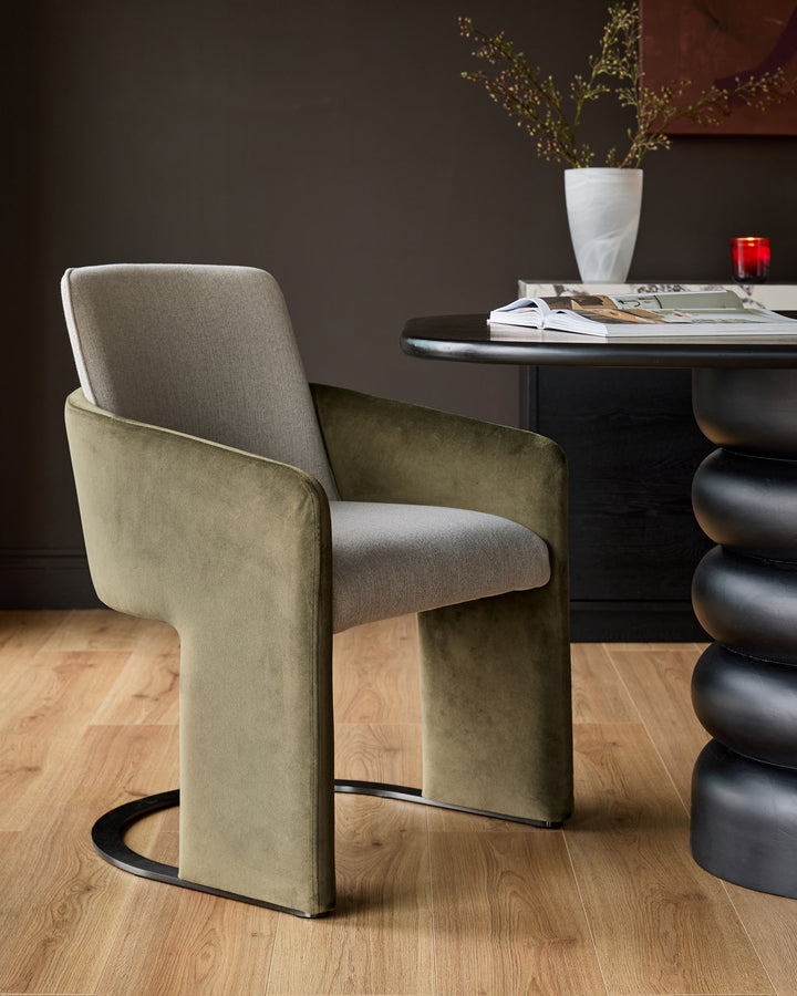 Wren cantilever dining chair in natural and olive green velvet fabric, shown at an angle in a styled interior setting.