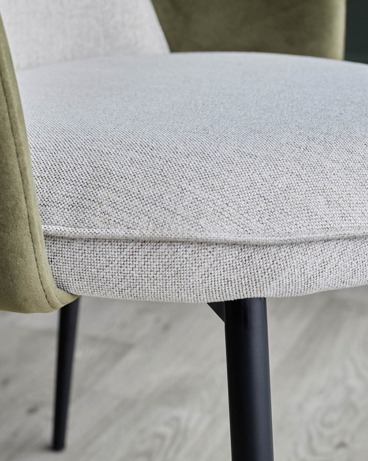 Close-up of an upholstered chair with neutral fabric and black legs, showcasing its texture and design.