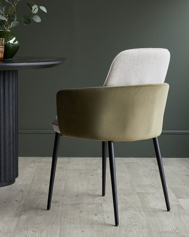 Stylish dining chair with a sleek, olive-green velvet back, neutral fabric seat and black metal legs next to a round table.