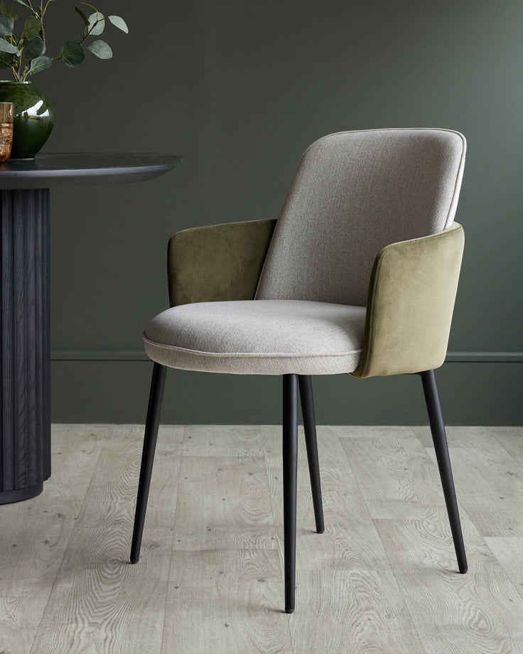 A stylish modern dining chair with a light grey fabric seat and backrest, and olive green armrests, sat on black legs.