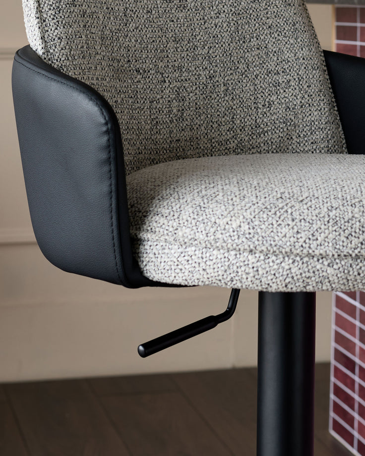 Wren gas lift bar stool showing grey fabric seat, black faux leather armrest and backrest detail, with black metal base.