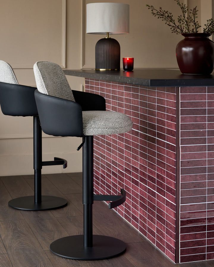 Wren gas lift bar stool in grey fabric and black faux leather, shown at burgundy tiled counter with rounded base.