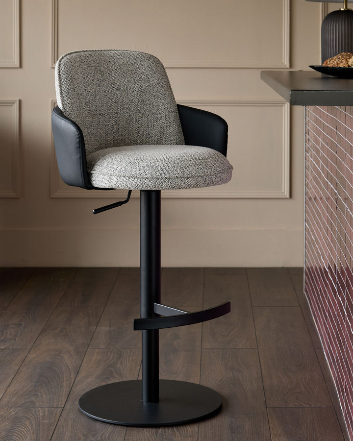 Wren gas lift bar stool with grey fabric seat and black faux leather back, mounted on black metal pedestal base.