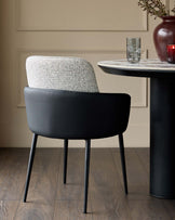Wren dining chair in grey fabric and black faux leather, shown at a round black table with marble top in a neutral interior.