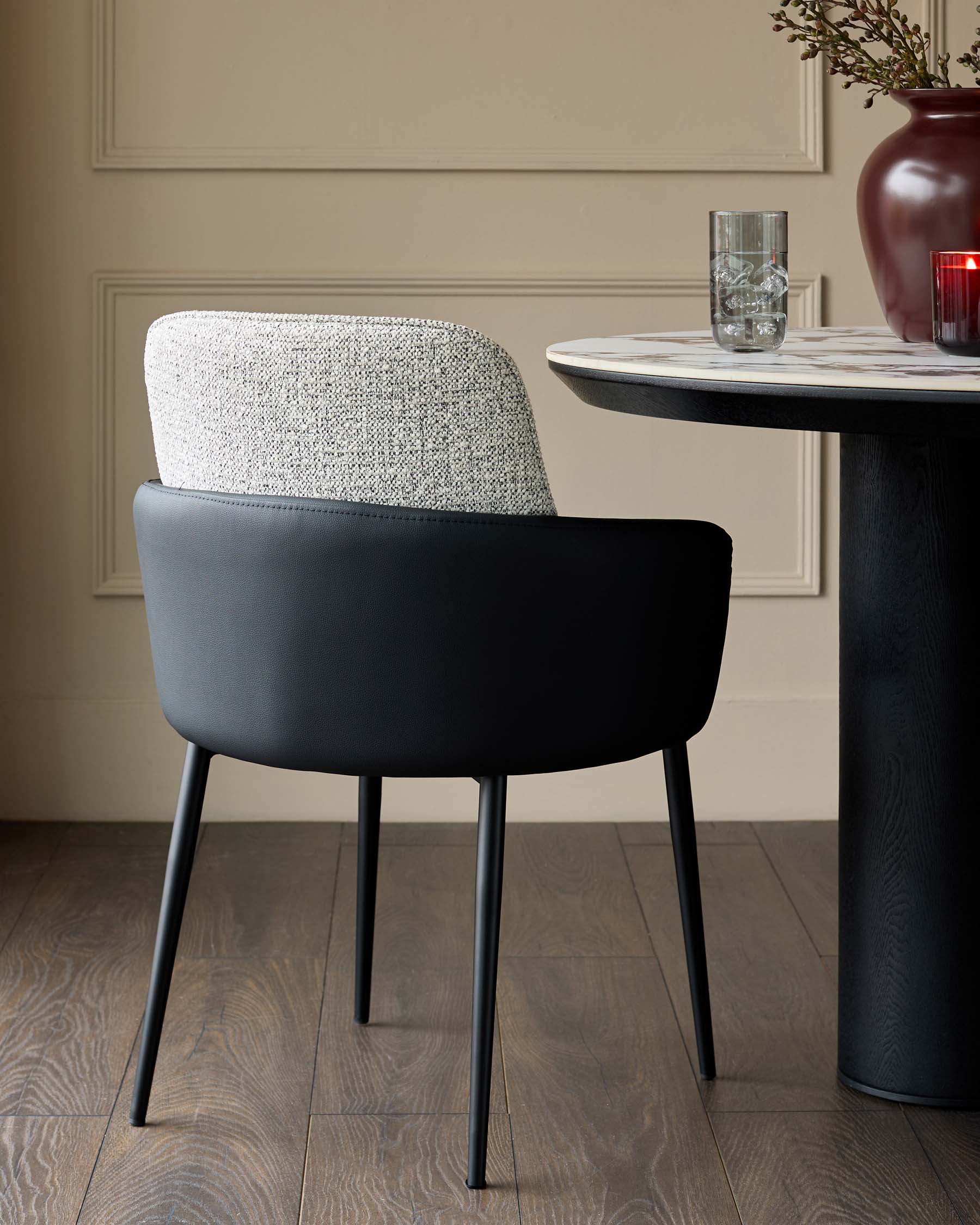 Wren dining chair in grey fabric and black faux leather, shown at a round black table with marble top in a neutral interior.