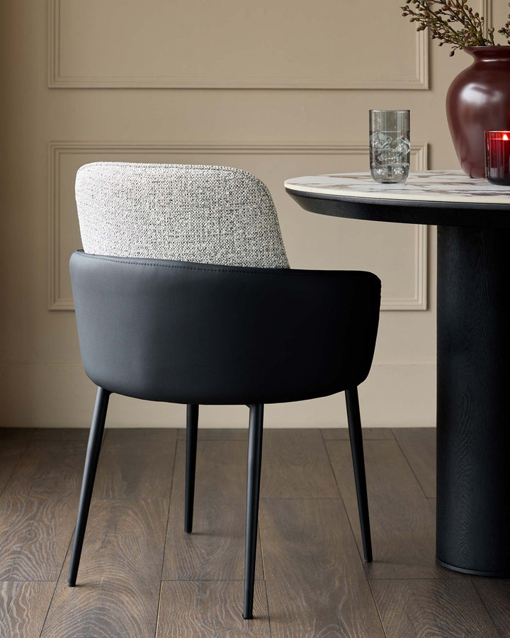 Wren dining chair in grey fabric and black faux leather, shown at a round black table with marble top in a neutral interior.