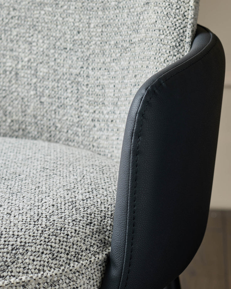Wren dining chair showing grey fabric seat with black faux leather armrest and curved edge detail.