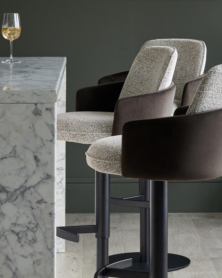 Stylish bar stools with dark arms and marble bar, plus a stemmed glass of white wine. Luxe and modern.