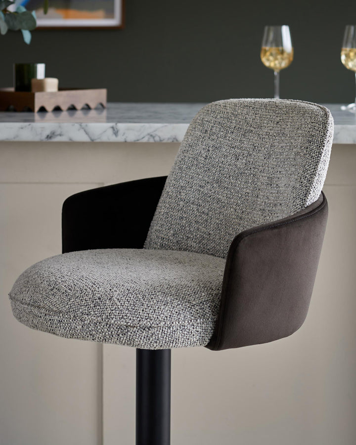 Grey tweed bar stool with dark brown arms and a black stand, placed against a bar setting with wine glasses.