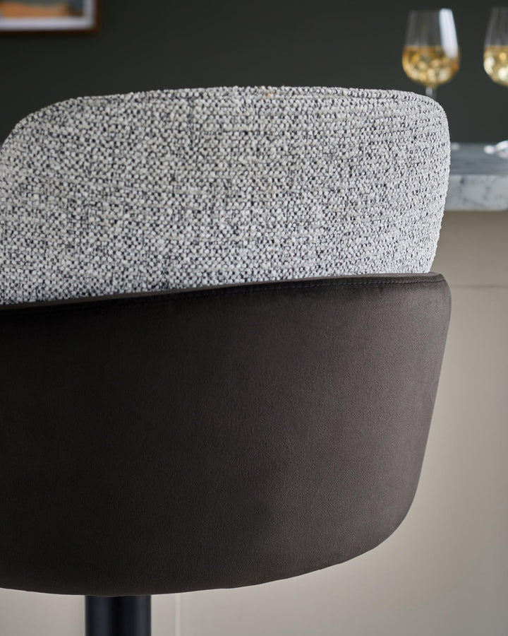 Close-up of a stylish bar stool with a textured light grey top and a dark brown leather-look base.