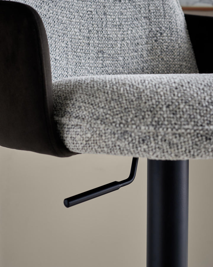Close-up of a stylish bar stool with a textured grey seat, sleek black frame and height adjustment lever.