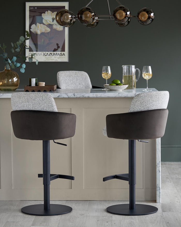 Two stylish bar stools with plush brown seats and patterned backs sit beneath a marble-topped counter and lighting fixture.