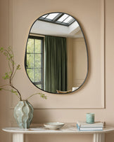 Black oval wall mirror with curved metal frame displayed above a marble console table with decorative accessories.