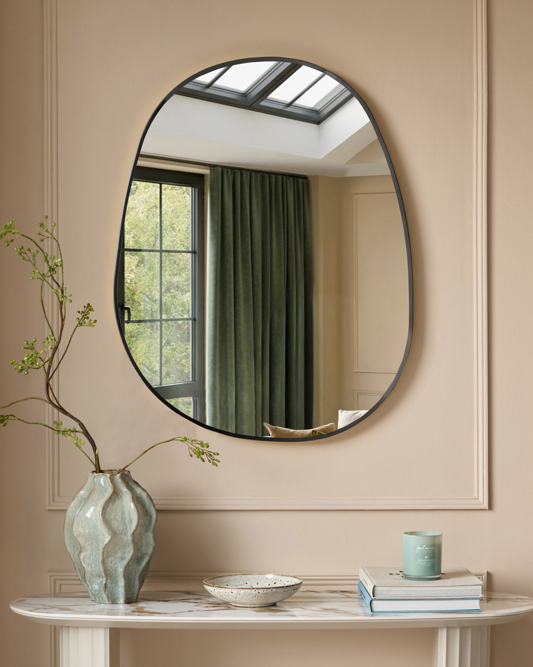 Black oval wall mirror with curved metal frame displayed above a marble console table with decorative accessories.
