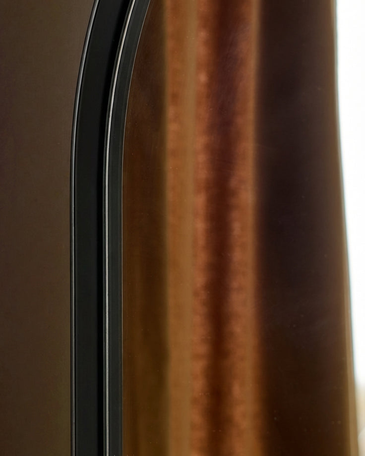 Black arched wall mirror with curved frame detail and bronze-toned background reflection.