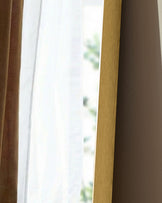 Gold rectangular leaner mirror with wooden frame, shown at an angle near a window with natural light.