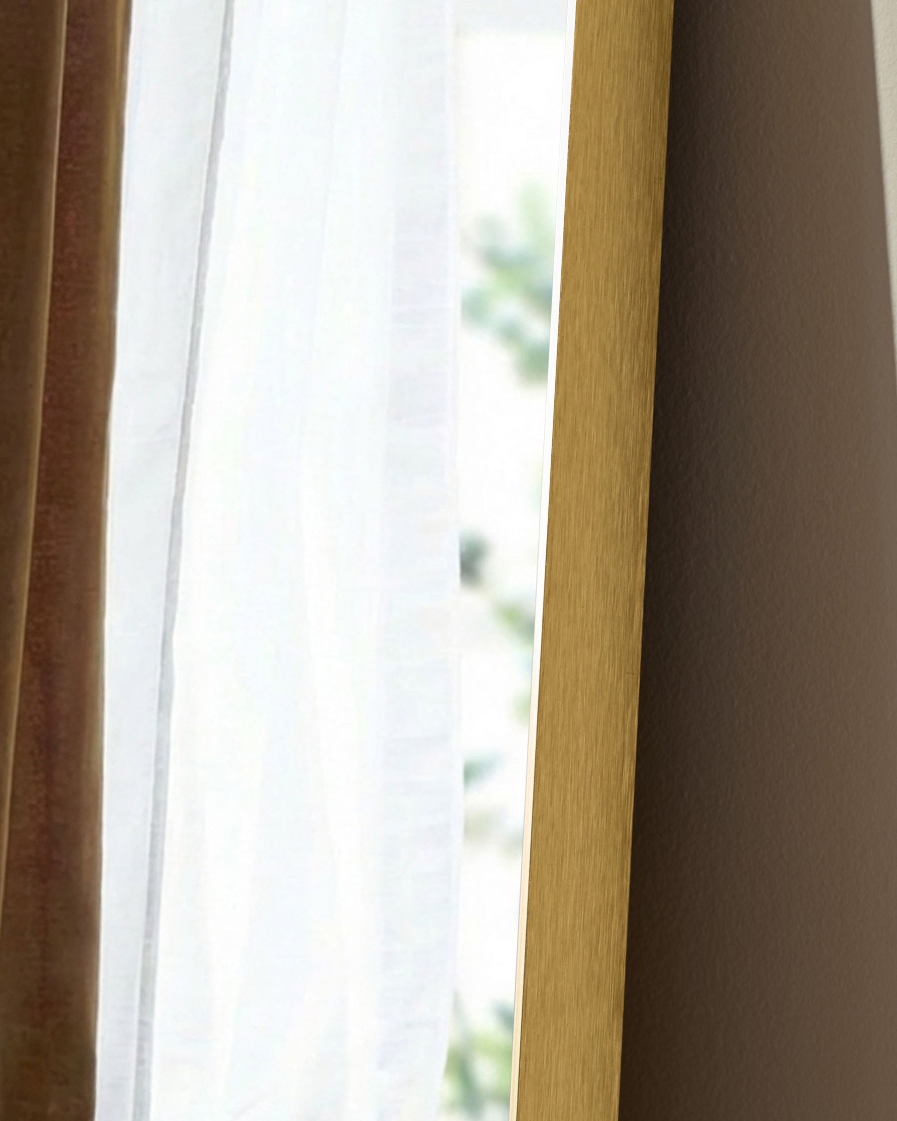 Gold rectangular leaner mirror with wooden frame, shown at an angle near a window with natural light.