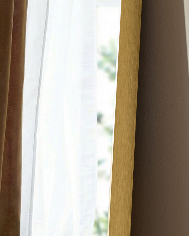 Gold rectangular leaner mirror with wooden frame, shown at an angle near a window with natural light.