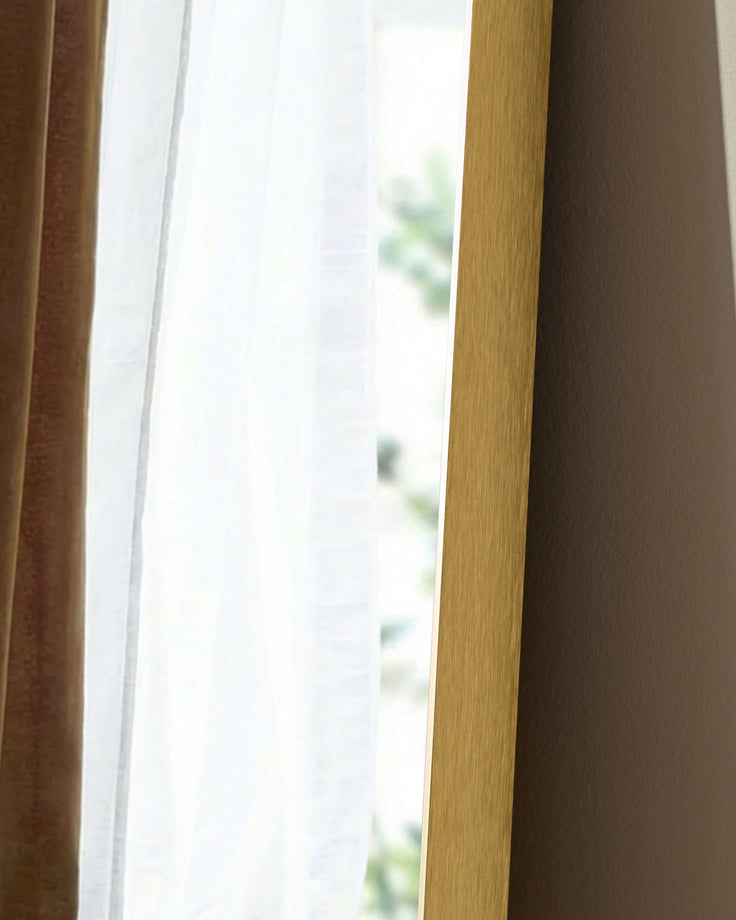 Gold rectangular leaner mirror with wooden frame, shown at an angle near a window with natural light.