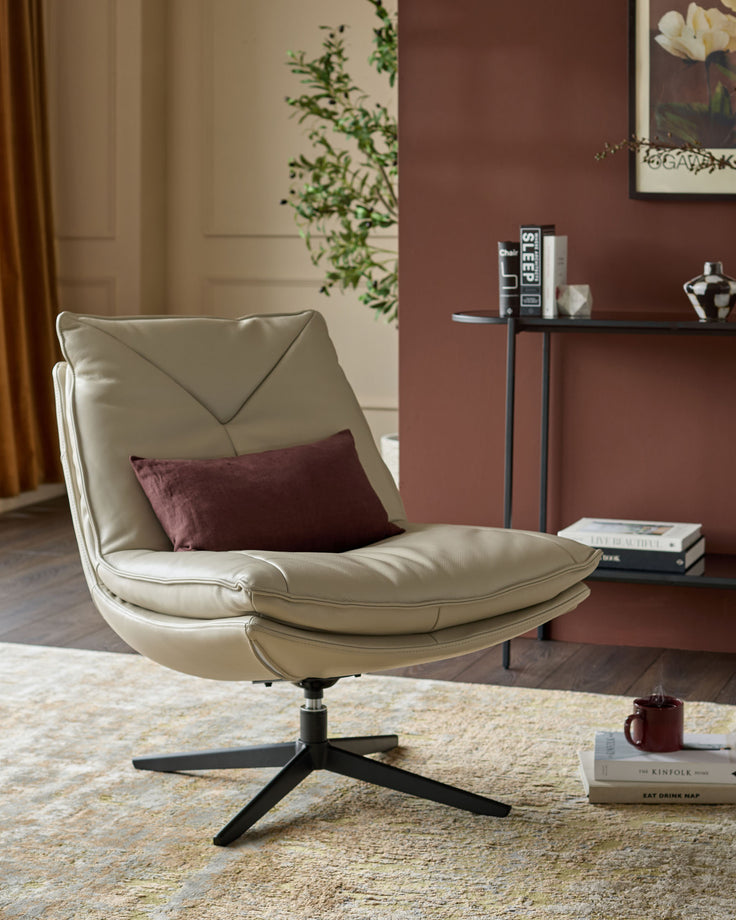 Cream leather swivel chair with curved backrest and burgundy pillow, black pedestal base, in modern living room setting.