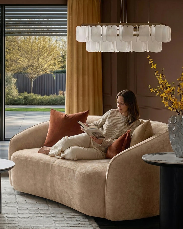 Champagne fabric 2-seater sofa with curved arms in a modern living room setting, styled with rust and cream pillows.