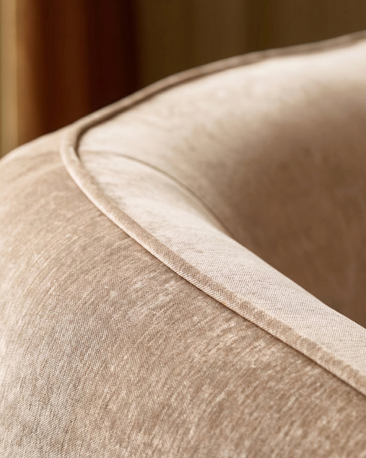 Zoey armchair in champagne fabric, close-up detail of curved armrest and stitching.
