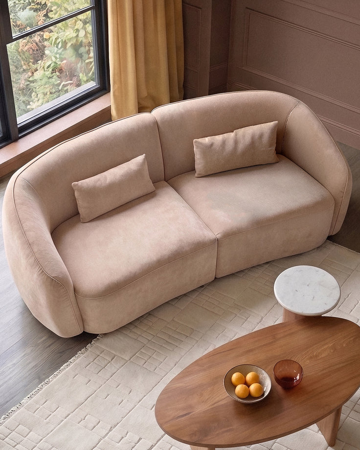 Champagne fabric 3-seater sofa with curved arms and two matching lumbar pillows, positioned in a modern living room.