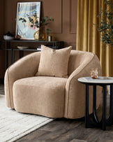 Champagne fabric Zoey armchair with curved design, shown in a styled living room setting with accent pillow and side table.