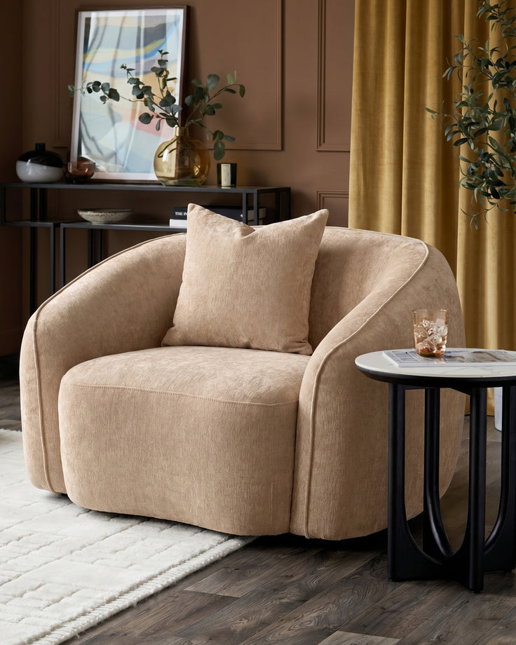 Champagne fabric Zoey armchair with curved design, shown in a styled living room setting with accent pillow and side table.