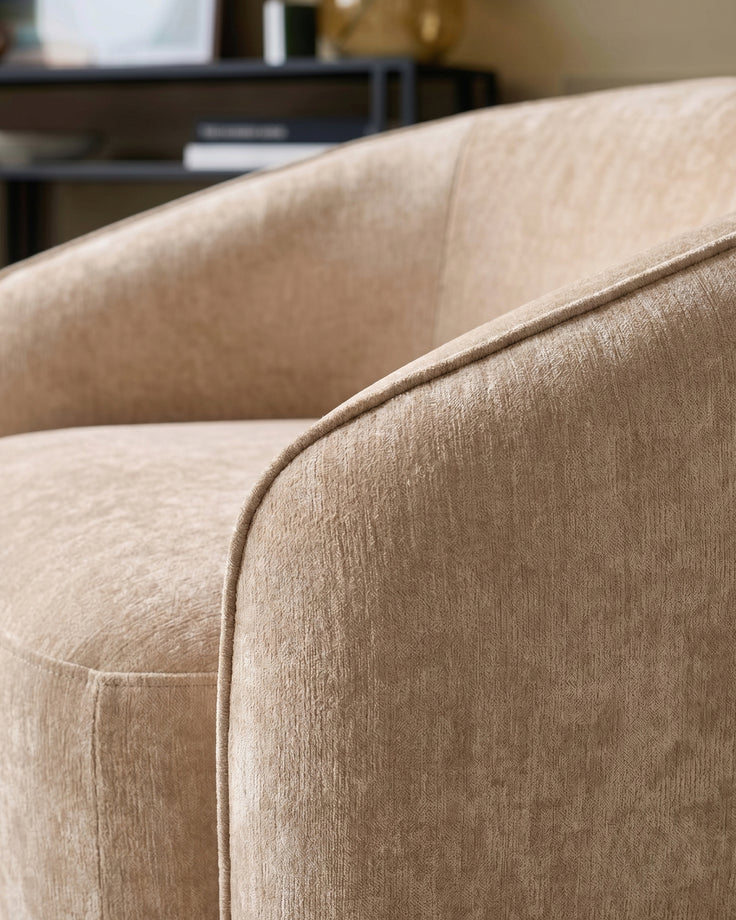 Close-up of Zoey armchair in champagne fabric, showing curved armrest and piping detail.