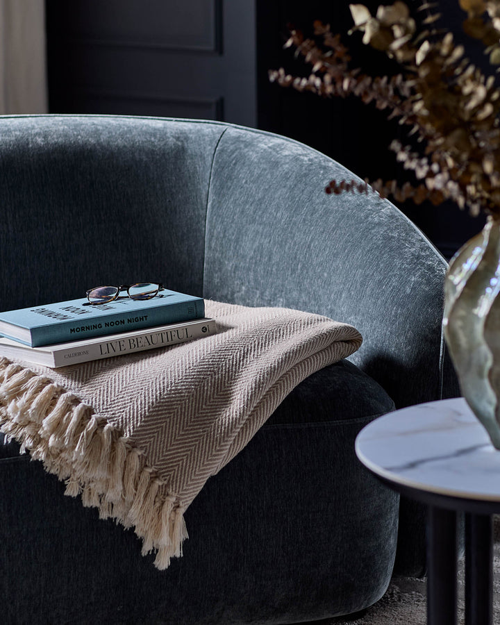 Zoey Armchair in blue-grey fabric, curved design with books and cream throw blanket draped over arm, styled setting.