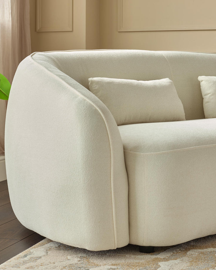 A modern, curved cream-coloured sofa with matching cushions, on a patterned rug. Minimalist design.