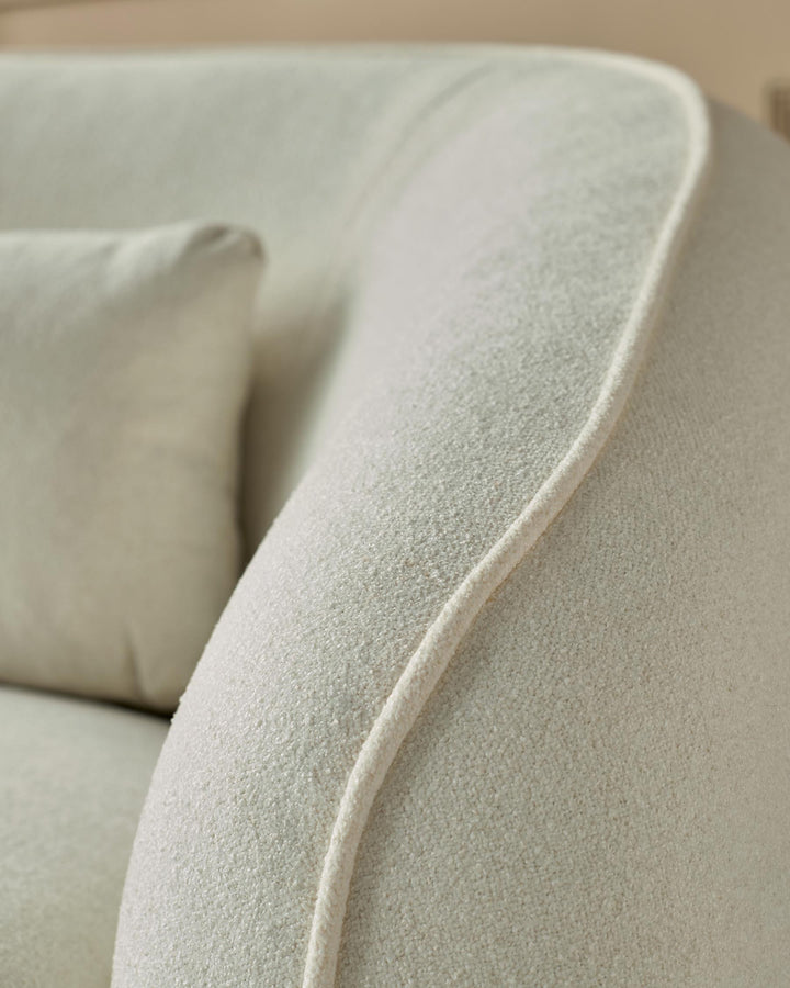 Close-up of a stylish, cream-coloured sofa with textured fabric and a piped seam design, showcasing its comfy cushion.