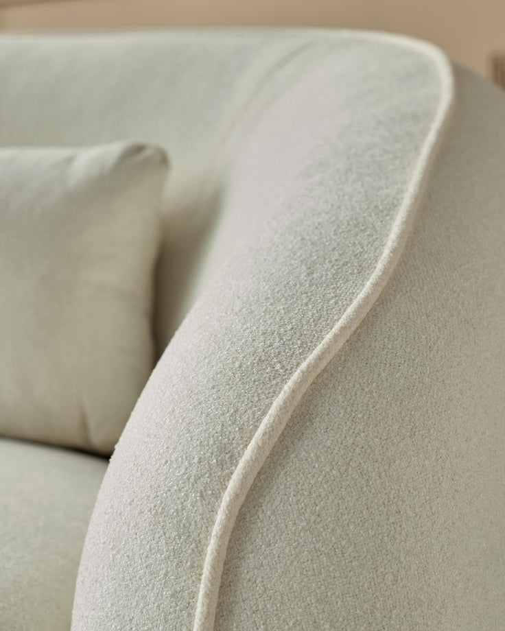Close-up of a stylish, cream-coloured sofa with textured fabric and a piped seam design, showcasing its comfy cushion.