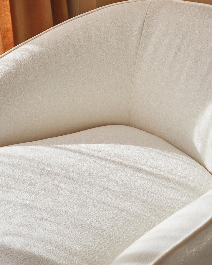 Close up of a cream boucle armchair. Soft lighting and gentle shadows add depth to the texture.