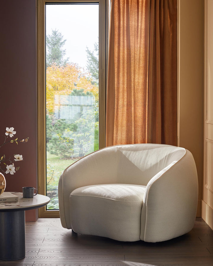 A stylish interior featuring an elegant cream armchair next to a side table and window.