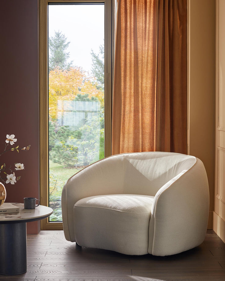 A stylish interior featuring an elegant cream armchair next to a side table and window.
