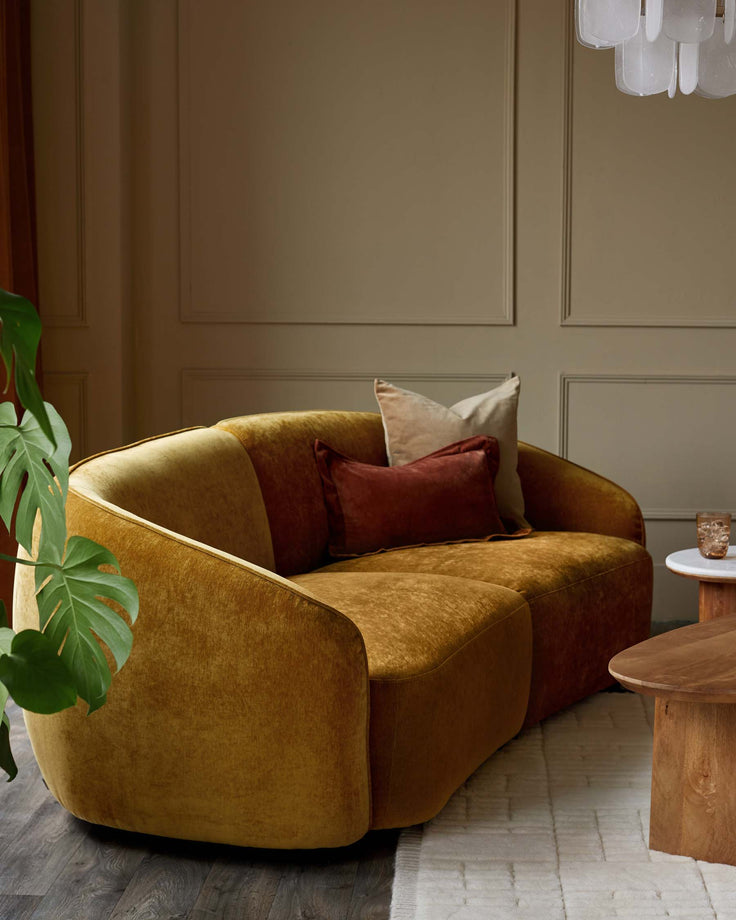 A mustard yellow two-seater sofa sits on a patterned rug with side tables and scatter cushions.