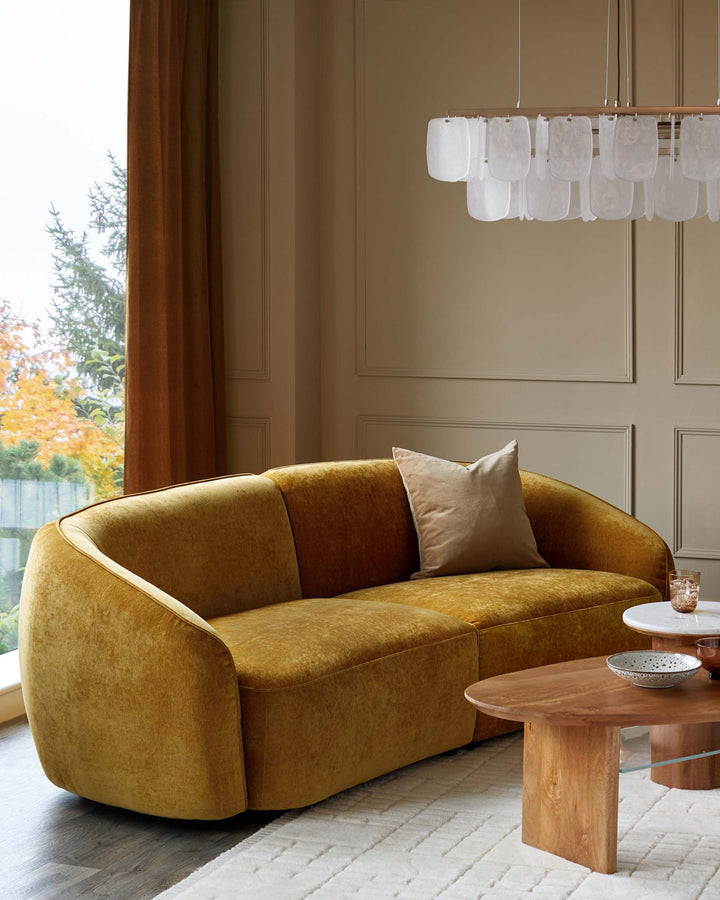 A gold velvet sofa, wooden coffee table and a layered white rug create a comfy and stylish living space.