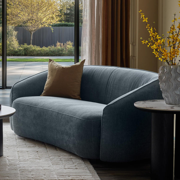 A stylish living room features a modern blue sofa with a brown cushion, complemented by marble-topped side tables.