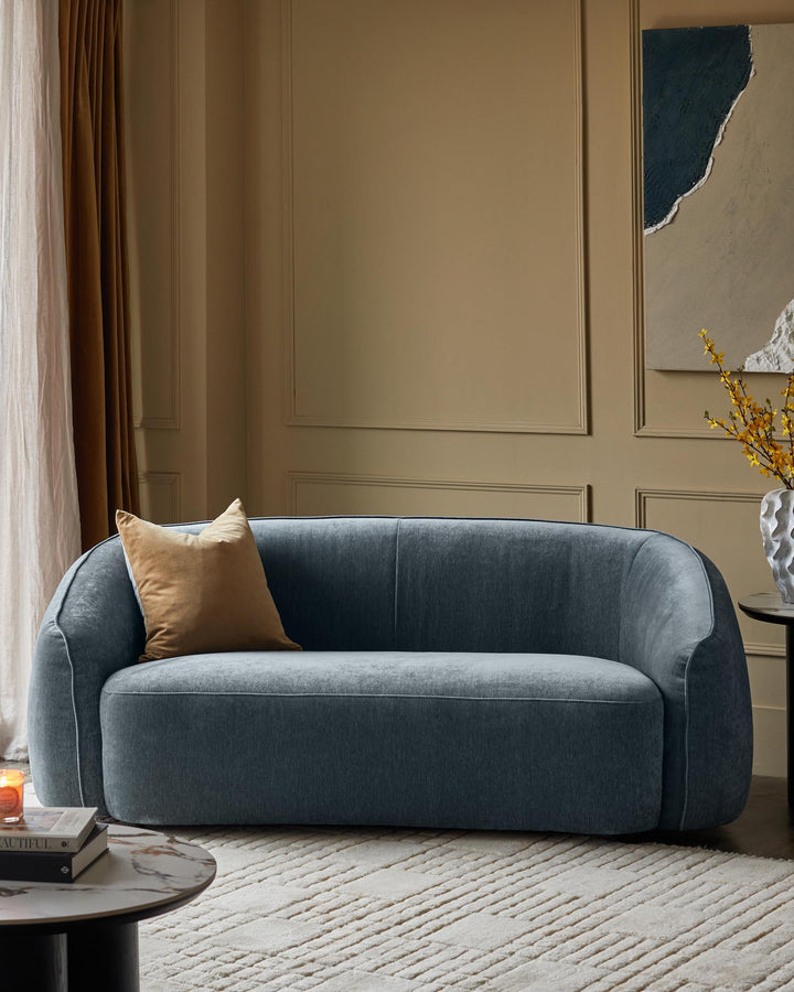 A stylish, curved blue sofa with a tan cushion sits on a patterned rug. Contemporary design for a modern living space.