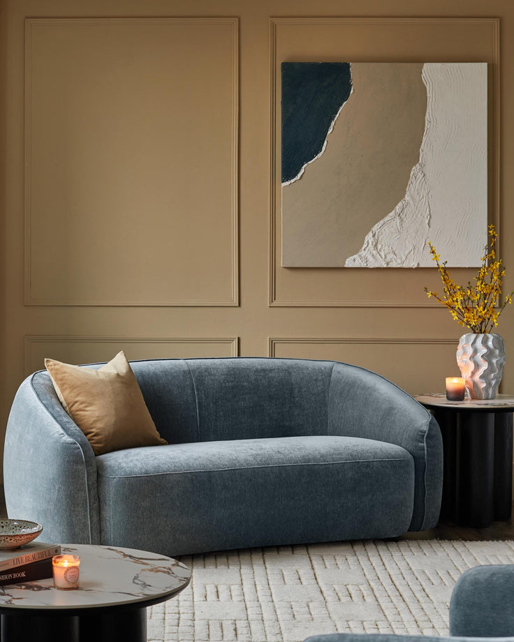 Stylish blue sofa with gold cushion, marble-topped side tables, decorative vase and framed art; modern living room furniture.