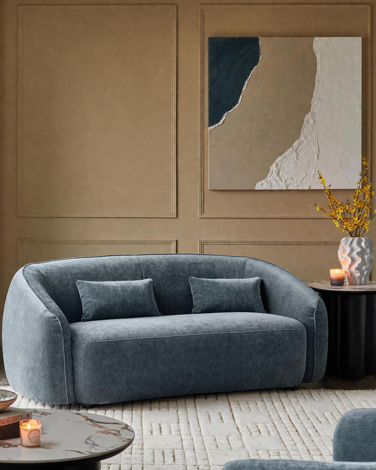 Zoey 2-seater sofa in blue-grey fabric with curved arms and two matching cushions in a neutral room setting.