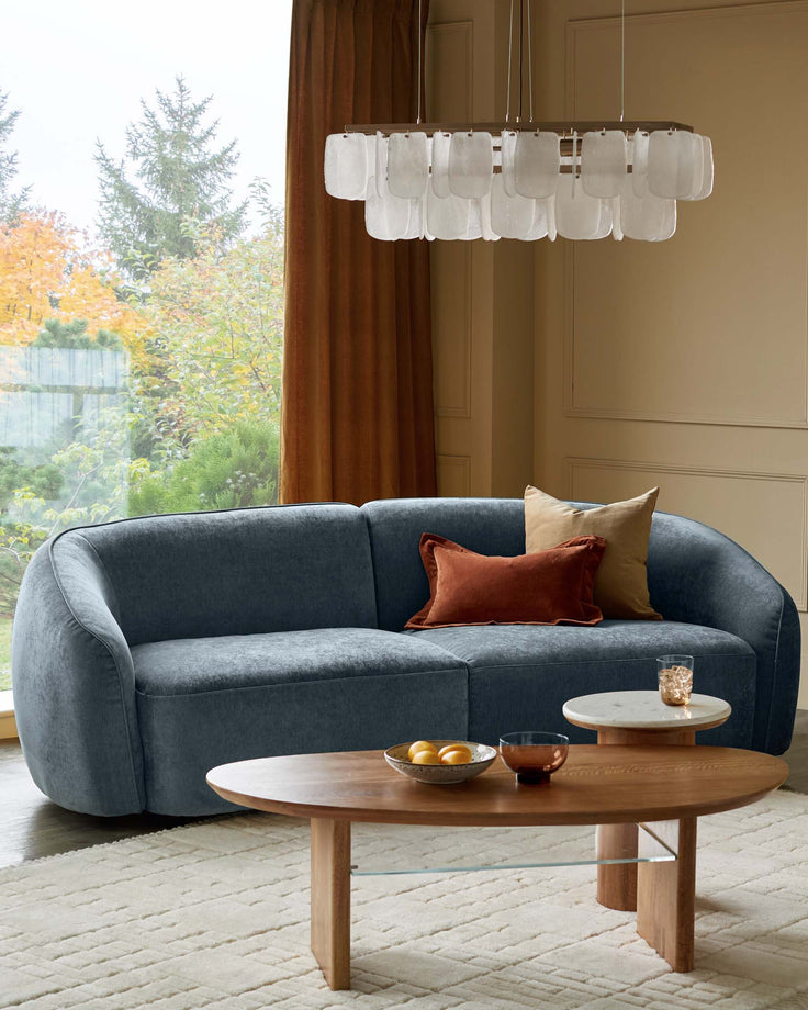 A contemporary living room setting featuring a stylish blue sofa, oval coffee table, and overhead lighting.