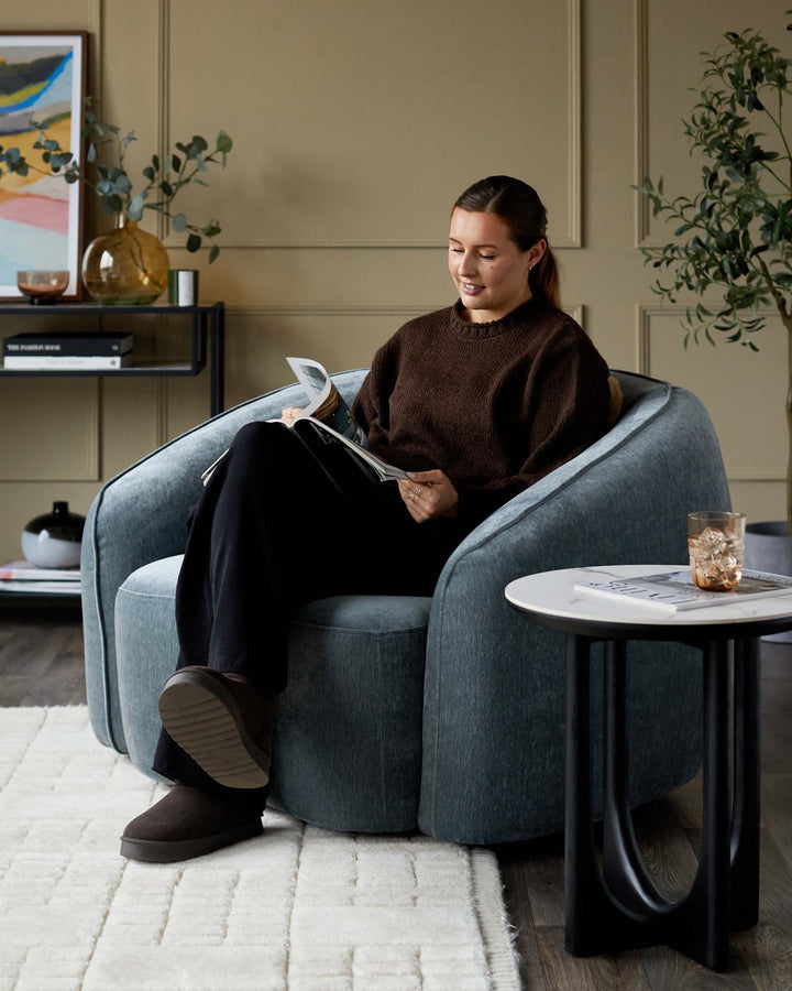 Stylish living room with a woman relaxing in a plush blue armchair next to a modern marble-top side table.